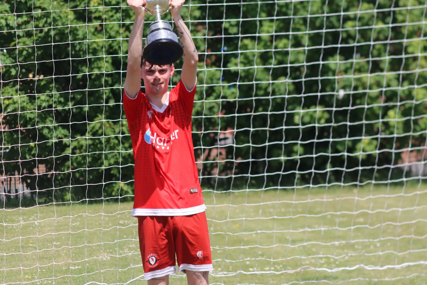Heron United player lifting the trophy in front of the net